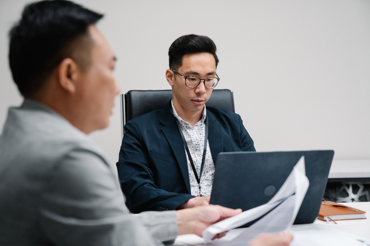 An image of two coworkers in the office. One is in the foreground and the other is working on a laptop in the background.